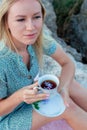 A woman sits on the seashore with glass in her hands.