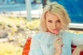 Woman blonde hair holding smelling a pink rose looking at you camera boyfriend husband sitting on red bench isolated city outdoors Royalty Free Stock Photo