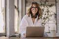 Attractive mid aged woman sitting at the table and using her laptop for work Royalty Free Stock Photo