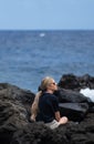 Woman with blonde hair sitting on the rocks near the sea looking Royalty Free Stock Photo