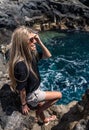 Woman with blonde hair and sunglasses sitting on the rocks near the sea Royalty Free Stock Photo
