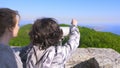 Woman blonde and her son teenager, travelers, looking through a telescope on top of a mountain.