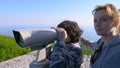 Woman blonde and her son teenager, travelers, looking through a telescope on top of a mountain.