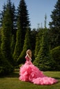 Woman with blonde locks wearing pink evening dress with fluffy skirt is posing in botanical garden on the grass Royalty Free Stock Photo