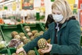 Woman blonde in a medical mask chooses fruit in a supermarket. Self-isolation in a pandemic