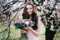 Woman in blooming trees. Woman with wedding bouquet in hands.