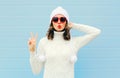 Woman blowing red lips makes air kiss wearing a heart shape sunglasses, knitted hat, sweater over blue Royalty Free Stock Photo