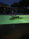 Woman on a blowup pool cacti in a lit swimming pool