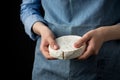 Woman in blue apron holding soft french camembert cheese on dark background Royalty Free Stock Photo