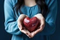 A woman with blue blouse holding a heart shaped apple in her hands