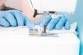 a woman in blue disposable medical gloves sews on a sewing machine a protective face mask made of cotton gray fabric