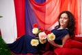 Woman in blue dress with long brunette curly hair and roses in hands indoors with red and blue background. Model posing Royalty Free Stock Photo