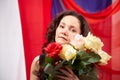 Woman in blue dress with long brunette curly hair and roses in hands indoors with red and blue background. Model posing Royalty Free Stock Photo