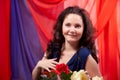 Woman in blue dress with long brunette curly hair and roses in hands indoors with red and blue background. Model posing Royalty Free Stock Photo