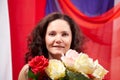 Woman in blue dress with long brunette curly hair and roses in hands indoors with red and blue background. Model posing Royalty Free Stock Photo