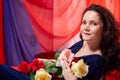 Woman in blue dress with long brunette curly hair and roses in hands indoors with red and blue background. Model posing Royalty Free Stock Photo