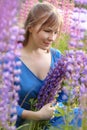 Woman in blue dress in purple lupines field. Meadow of violet flowers in the summer. Girl with long hair holding a lupine bouquet Royalty Free Stock Photo