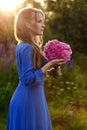 Woman in blue dress in purple lupines field. Meadow of violet flowers in the summer. Girl with long hair holding a lupine bouquet Royalty Free Stock Photo