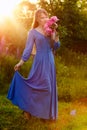 Woman in blue dress in purple lupines field. Meadow of violet flowers in the summer. Girl with long hair holding a lupine bouquet Royalty Free Stock Photo