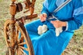 A woman in a blue dress spinning a spindle. Retro wooden wheel for thread making Royalty Free Stock Photo