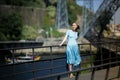 A woman in a blue dress stands on the boardwalk of the riverfront.