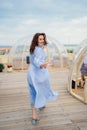 woman in a blue dress walks in a cafe in the shape of a igloo on roof.