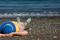 Woman in blue panama and blue sneakers is relaxing on seashore, lying on her back on pebble beach. Royalty Free Stock Photo