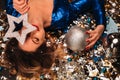 A woman in a blue sequined dress smiles and lies on the floor under a falling multicolored confetti