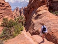 Woman in blue shirt, hat in her hand and backpack hiking down a rocky path with in the Arches National Park, Utah, USA