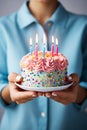 Woman in blue shirt holding a birthday cake with lighted candles