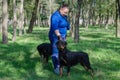 A woman in a blue sports uniform and two black dogs standing on green grass. Handler and adult female Rottweiler