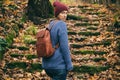 Woman in blue sweater, red knitted hat and with leather backpack walking on autumn park or forest. Slow life, back to nature,