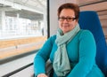 Woman in a blue sweater and scarf with glasses travels in a train.