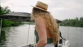 Woman boards boat, ready for lake excursion, straw on, wavy hair flow. Leisure activity, embark on tranquil waters