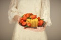 Woman, boho bride holding little cake on a plate with strawberries