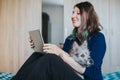 Woman bonding with friends during quarantine indoors with her funny pet. Female using tablet