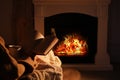 Woman with book and cup near fireplace indoors, closeup. Cozy atmosphere Royalty Free Stock Photo