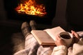 Woman with book and cup near fireplace indoors, closeup. Cozy atmosphere Royalty Free Stock Photo