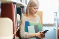 Woman, books in library and smartphone, education and research on university website for studying and knowledge. Student