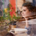 Woman, books and thinking by window in restaurant for creative idea, reading inspiration and learning for knowledge