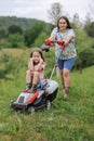 A woman in boots with her child in the form of a game mows the grass with a lawnmower in the garden Royalty Free Stock Photo