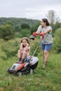 A woman in boots with her child in the form of a game mows the grass with a lawnmower in the garden Royalty Free Stock Photo