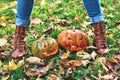 Woman in boots stands over Halloween pumpkins outdoor in the autumn park