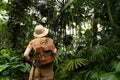 Woman botanist in greenhouse, back view. Naturalist with backpack walks in the rainforest surrounded by palms. Jungle tourist