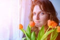 Woman with a bouquet of red tulips window. Young girl close-up with a bouquet of flowers. Spring portrait with scarlet tulips