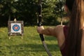 Woman with bow and arrow aiming at archery target in park, closeup