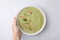 Woman with bowl of delicious broccoli cream soup at table, top view