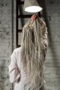 Woman with braids, in shirt. Young woman sits with her back under the light of chandeliers