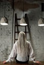 Woman with braids, in shirt. Young woman sits with her back under the light of chandeliers