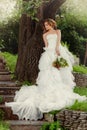 Woman bride in a wedding dress relaxes standing by a large tree.